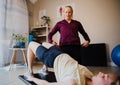 Physio-therapist corrects alignment of patient attempting bridge position lying on mat in exercise studio Royalty Free Stock Photo