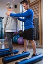 Physiotherapist assisting senior woman in performing exercise on foam roll Royalty Free Stock Photo