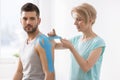 Physiotherapist covering selected fragments of young man`s body with special structure patches during kinesiotaping therapy Royalty Free Stock Photo