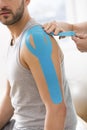 Physiotherapist covering selected fragments of man`s body with special structure patches during kinesiotaping therapy Royalty Free Stock Photo