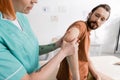 physiotherapist flexing painful elbow of bearded Royalty Free Stock Photo