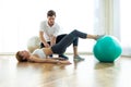 Physiotherapist helping patient to do exercise on fitness ball in physio room