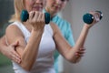 Physiotherapist helping senior woman to lift hand weights