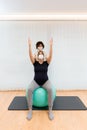 Physiotherapist helping to stretch the arms of a pregnant woman to exercise sitting on a fitness ball