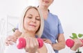 A physiotherapist helps an older woman recover from an injury through exercise with dumbbells.