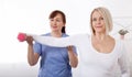 A physiotherapist helps an older woman recover from an injury through exercise with dumbbells.