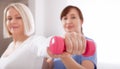 A physiotherapist helps an older woman recover from an injury through exercise with dumbbells.