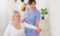 A physiotherapist helps an older woman recover from an injury through exercise with dumbbells.