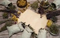 Paper blank surrounded by collection, a mixture of various dried herbs in bundles, linen bags and cups on a wooden background.