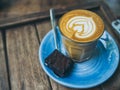 Piccolo Latte coffee topping with flower art from milk in small glass with a piece of homemade brownies cake on blue ceramic plate