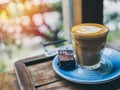 Piccolo Latte coffee topping with flower art from milk in small glass with a piece of homemade brownies cake on blue ceramic plate