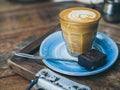 Piccolo Latte coffee topping with flower art from milk in small glass with a piece of homemade brownies cake on blue ceramic plate