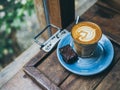 Piccolo Latte coffee topping with flower art from milk in small glass with a piece of homemade brownies cake on blue ceramic plate