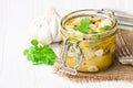 Pickled artichoke with garlic in a glass jar on white wooden ta