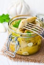 Pickled artichoke with garlic in a glass jar on white wooden ta