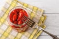 Pickled baby red hot pepper on a fork over open glass jar on a white wooden table. Marinated pod of small hot pepper close-up. Royalty Free Stock Photo