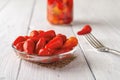 Pickled baby red hot peppers on a glass saucer over white wooden table. Marinated pods of small hot pepper close-up. Fermented