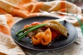 Pickled bell peppers of different colors, on a black matte plate, decorated with green onions, cutlery and a cloth napkin on