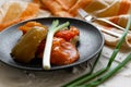 Pickled bell peppers of different colors, on a black matte plate, decorated with green onions, cutlery and a cloth napkin on