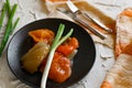 Pickled bell peppers of different colors, on a black matte plate, decorated with green onions, cutlery and a cloth napkin on