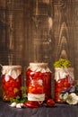 Pickled cherry tomatoes in jars, spices and herbs on a wooden background, space for text