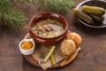 Pickled cucumber soup with pork and pearl barley and bread bun on wooden table Royalty Free Stock Photo