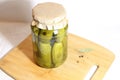 Pickled cucumbers with spices in glass jar on wooden bord with white baclground