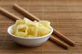 Pickled ginger slices in white ceramic bowl on bamboo mat next t