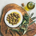 Pickled green Medoterranean olives and olive-tree branch on wooden board