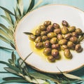 Pickled olives in oil and olive-tree branch over blue background Royalty Free Stock Photo