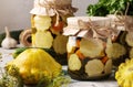 Pickled patissons, cucumbers with carrots and garlic in glass jars and fresh ingredients on a light gray background, Closeup Royalty Free Stock Photo