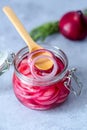 Pickled red onion rings on a wooden spoon on a glass jar. Appetizer, condiment or topping. Healthy fermented food.