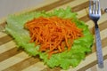 Pickled sliced carrot on a sheet of salad on a wooden board.