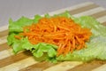 Pickled sliced carrot on a sheet of salad on a wooden board.