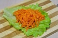 Pickled sliced carrot on a sheet of salad on a wooden board.