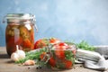 Pickled tomatoes in glass jars and products on table against blue background, space for text Royalty Free Stock Photo