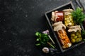 Pickled vegetables and mushrooms in glass jars in Wooden box on black stone background. Royalty Free Stock Photo