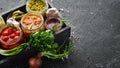 Pickled vegetables and mushrooms in glass jars in Wooden box on black stone background. Royalty Free Stock Photo