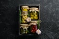 Pickled vegetables and mushrooms in glass jars in Wooden box on black stone background. Royalty Free Stock Photo