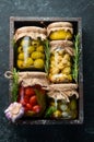 Pickled vegetables and mushrooms in glass jars in Wooden box on black stone background. Royalty Free Stock Photo