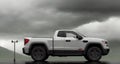 A pickup truck is driving down the road. Dark dramatic landscape as background, gloomy sky with rainy clouds, forest and Royalty Free Stock Photo