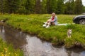 A picnic on the bank of a mountain river with green grass and yellow flowers against the background of coniferous trees and a blue Royalty Free Stock Photo