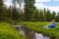 A picnic on the bank of a mountain river with green grass and yellow flowers against the background of coniferous trees and a blue Royalty Free Stock Photo