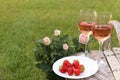 Picnic basket with glasses of delicious rose wine, strawberries and flowers outdoors, space for text