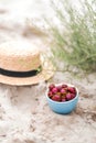 Picnic on beach, cherries in blue plate, straw hat on background Royalty Free Stock Photo