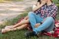 picnic. a guy and a girl are sitting on a plaid veil on the grass, hugging and kissing. a man in a plaid shirt and jeans, with a w Royalty Free Stock Photo