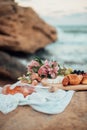 Picnic on large stones on the beach. A wooden plate with fruit and cheese, flowers and a bottle of rose wine Royalty Free Stock Photo