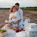 Picnic, love, tenderness. The couple sits on a plaid. A man embraces pregnant woman, with his hands on her tummy. Royalty Free Stock Photo