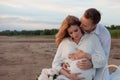 Picnic, love, tenderness. The couple sits on a plaid. A man embraces pregnant woman, with his hands on her tummy.