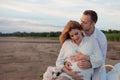 Picnic, love, tenderness. The couple sits on a plaid. A man embraces pregnant woman, with his hands on her tummy. Royalty Free Stock Photo